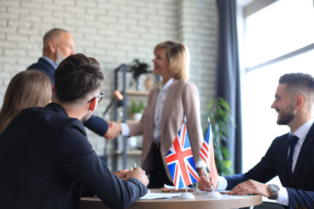 Profissionais em reunião com bandeiras do Reino Unido e EUA, representando testes de inglês para processo seletivo.