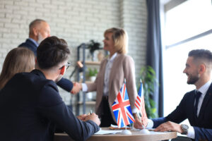 Profissionais em reunião com bandeiras do Reino Unido e EUA, representando testes de inglês para processo seletivo.