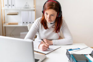 mulher em ambiente claro escevendo e realizando o toeic link na frente de um notebook