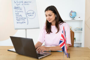 professora de inglês em ambiente escolar sentada na frente do computador pesquisando sobre o toeic para professores de inglês